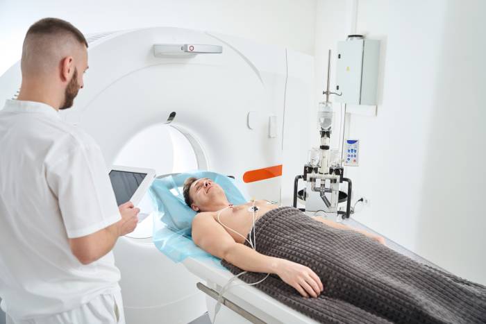 Image of a CT room with a male radiographer monitoring a person before undergoing an ECG-gated coronary CT angiography.