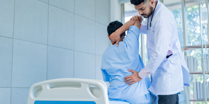 A physiotherapist explains stretching exercises to a patient with back pain during treatment in a hospital.